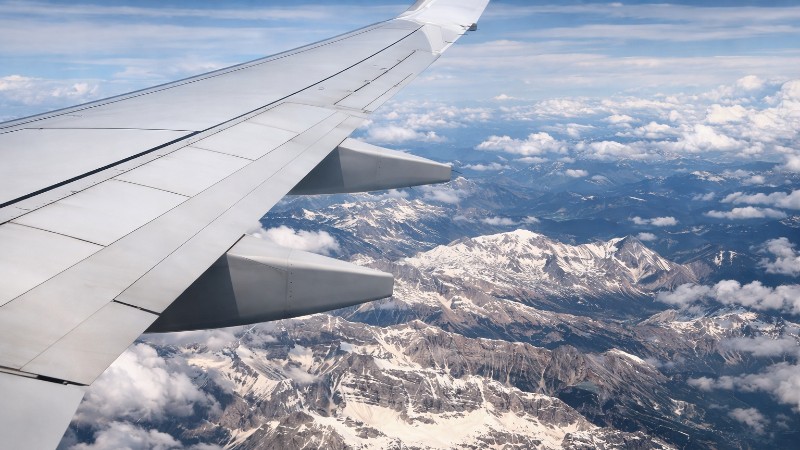 Airplane wing over snow-capped mountains